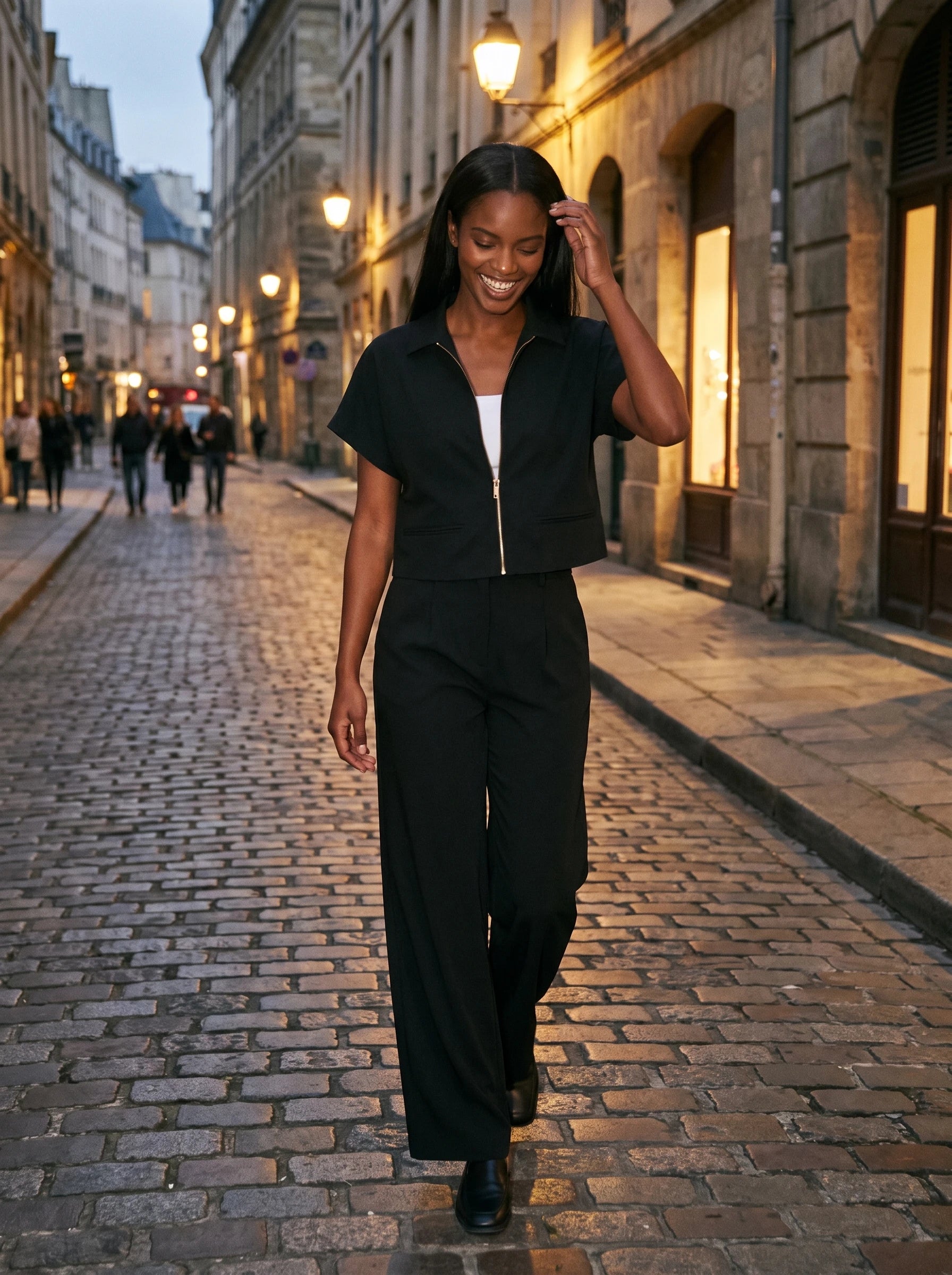 Veste courte zippée noire Gilberte, portée dans une rue pavée au crépuscule