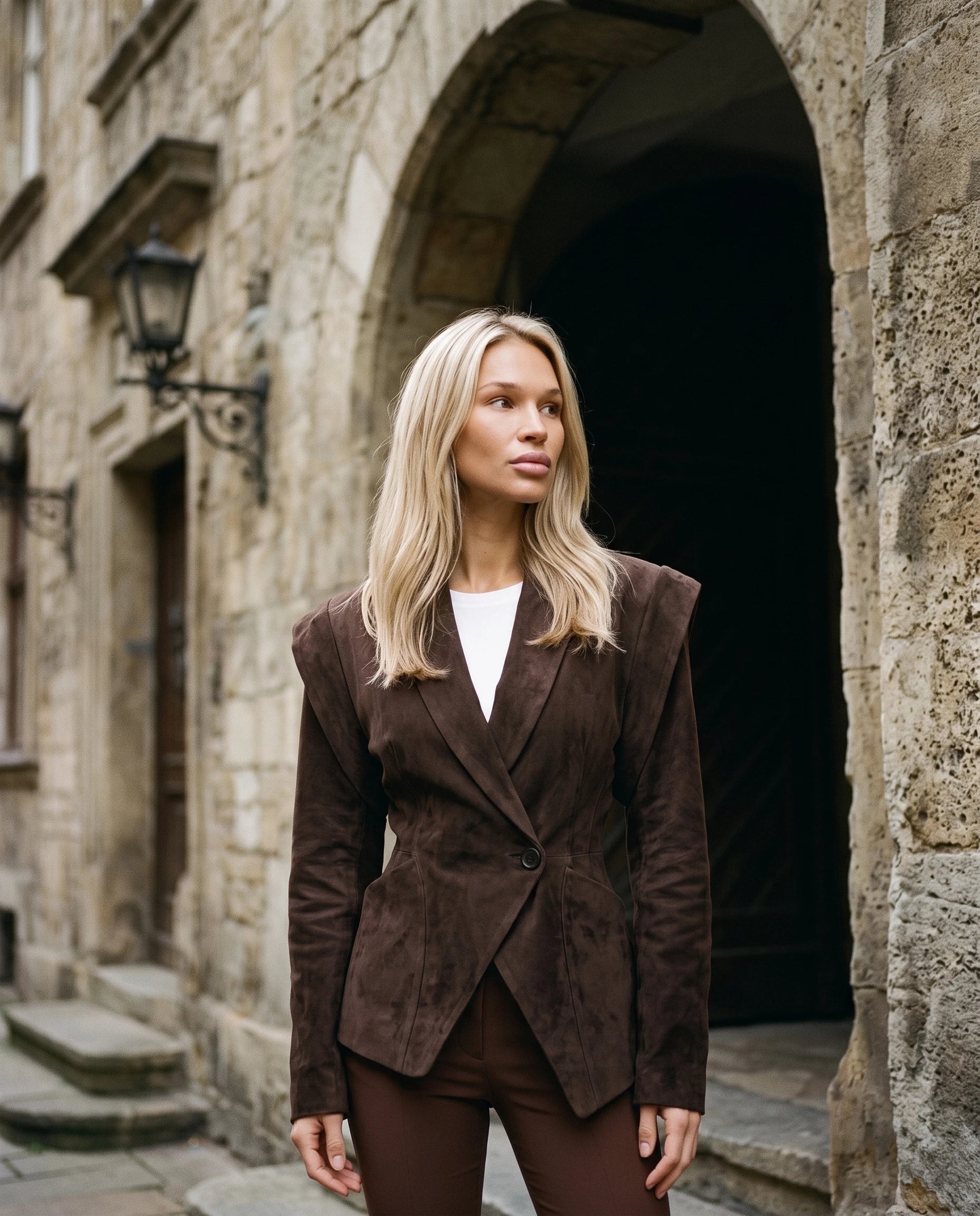 Veste en suédine cintrée chocolat Adeline, devant un porche en pierre ancienne