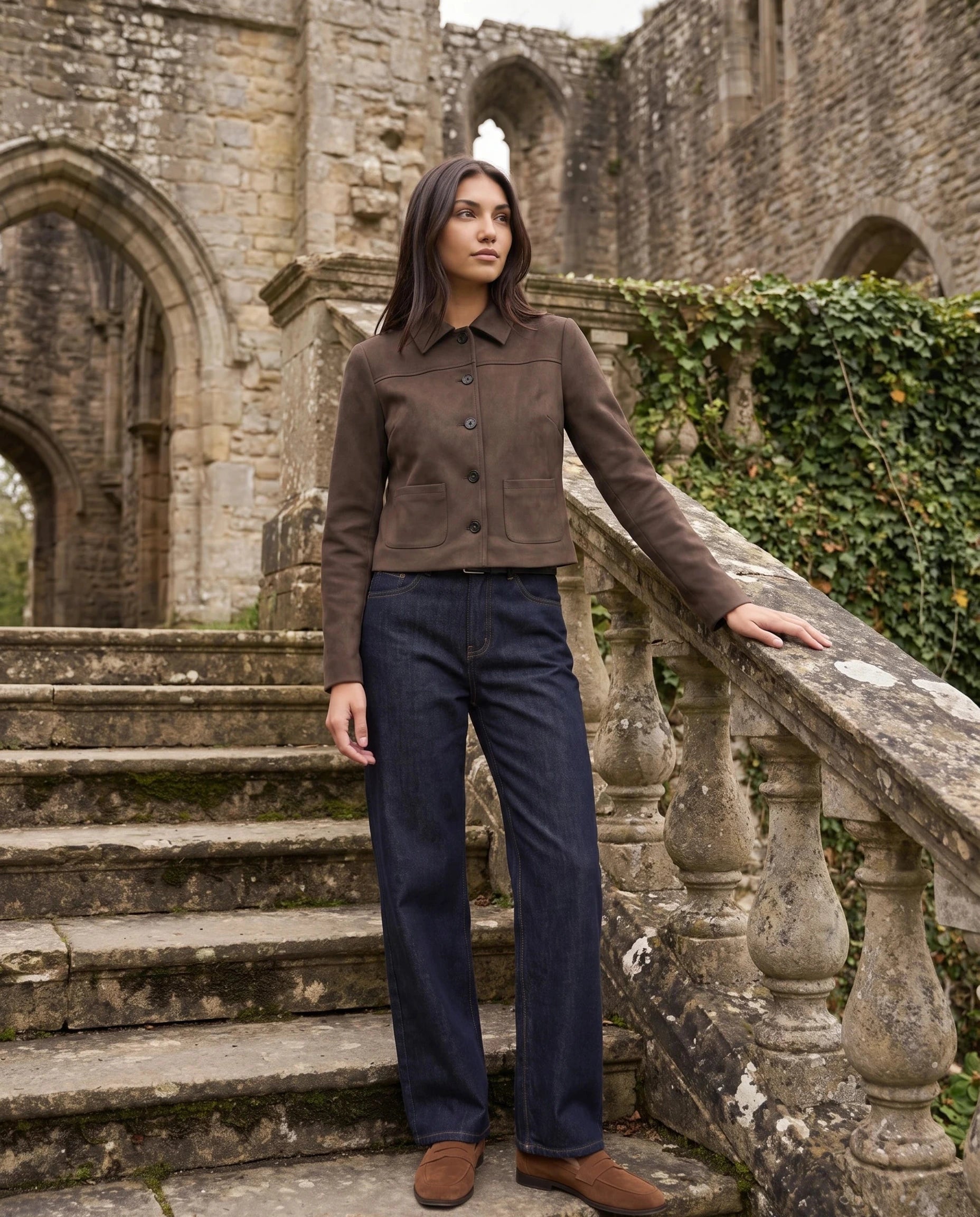 Veste en suédine brun cacao Pélagie, portée sur l'escalier de pierre d'une abbaye