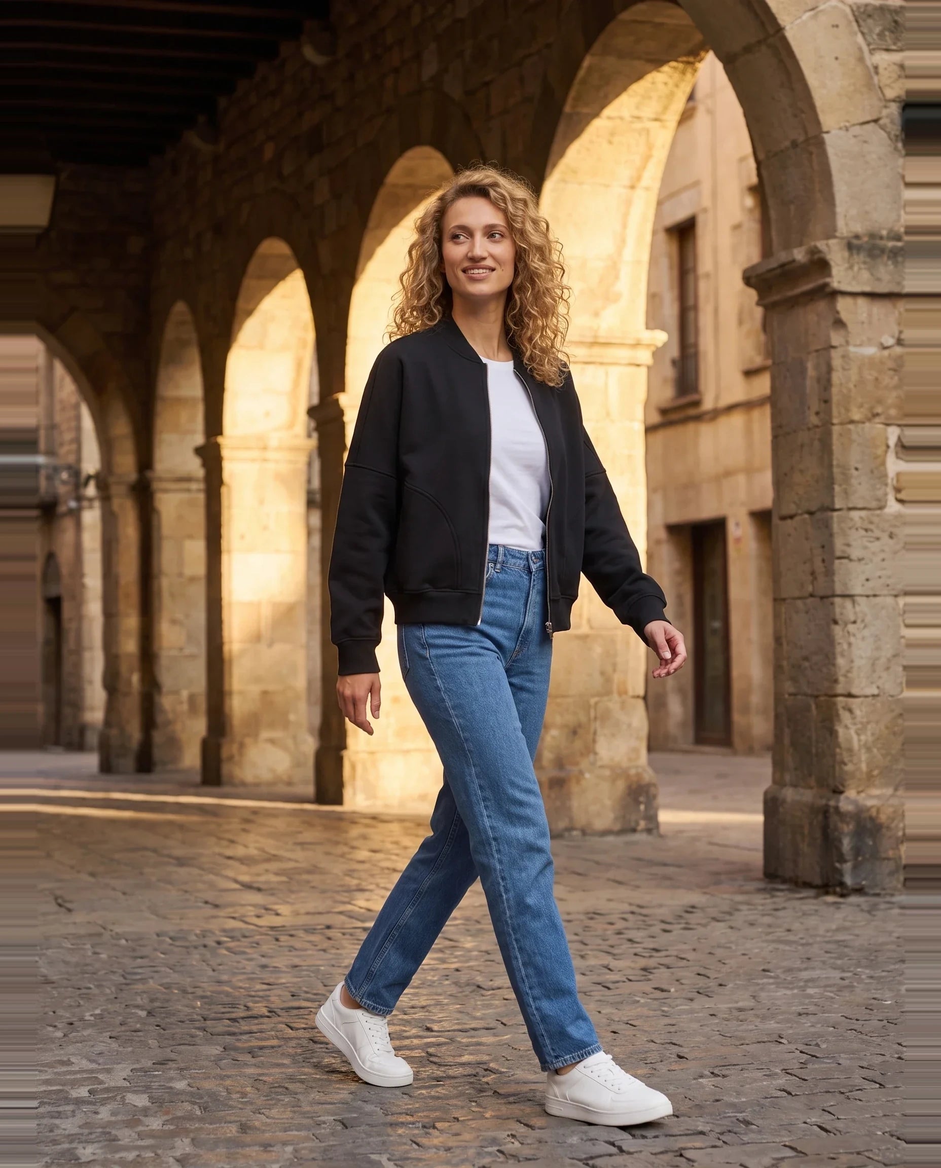 Bomber en molleton noir Denise, porté dans une rue aux arcades de pierre