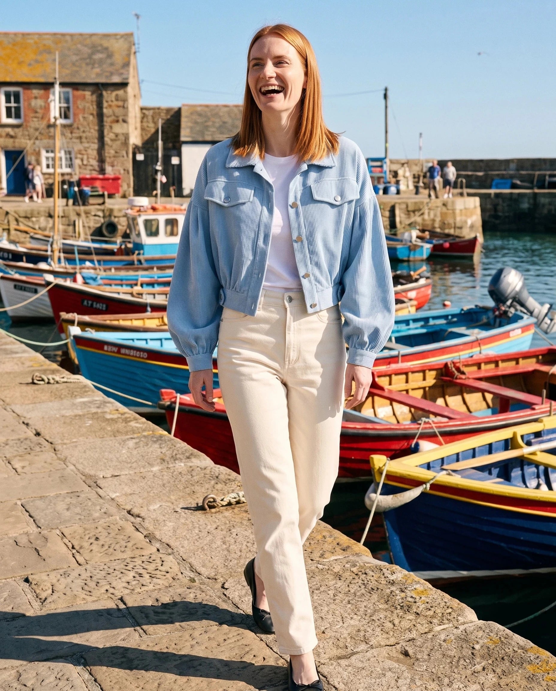 Veste en velours côtelé bleu ciel Yvette, portée sur un quai aux barques colorées