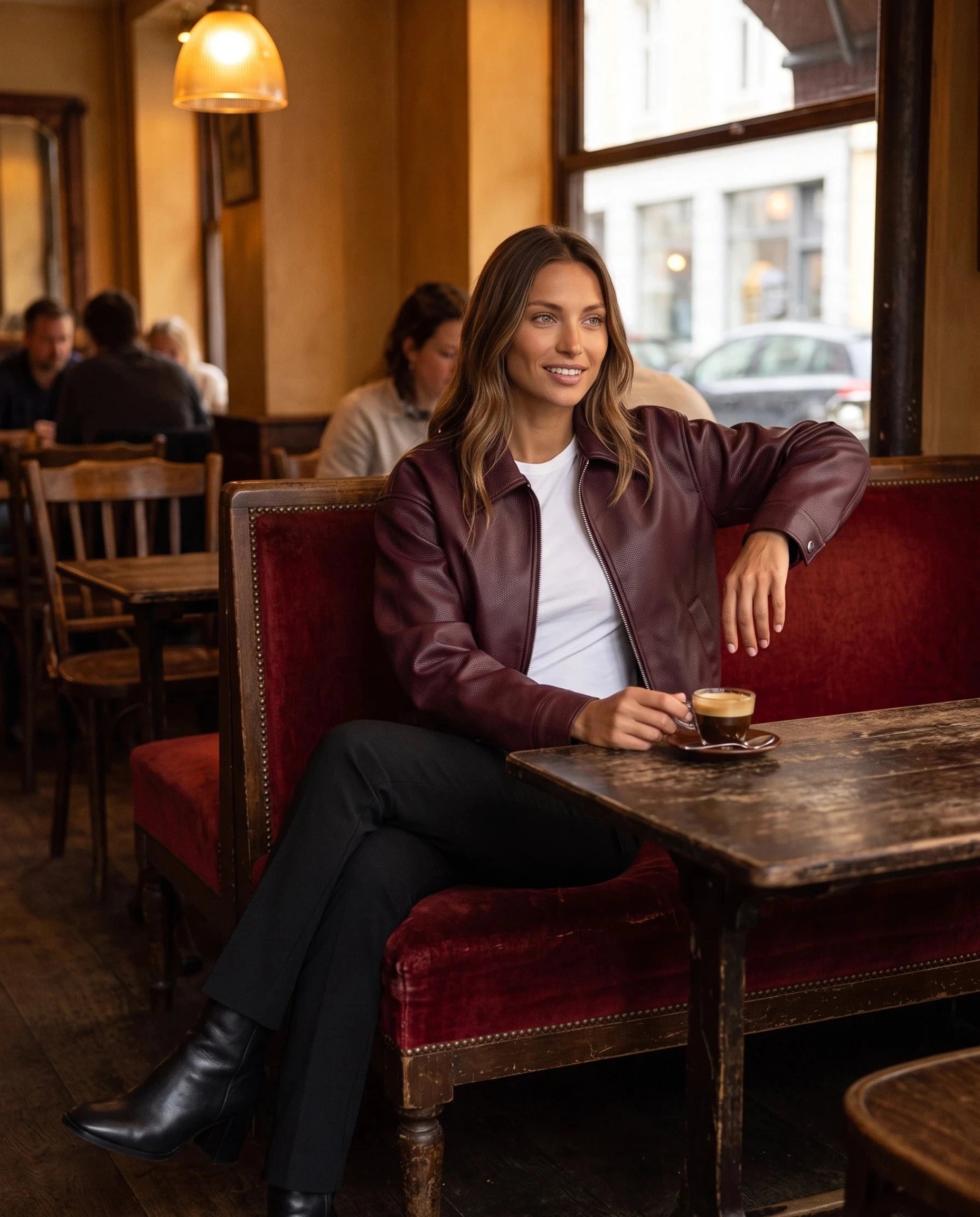 Veste effet cuir bordeaux Louane, portée sur une banquette de café