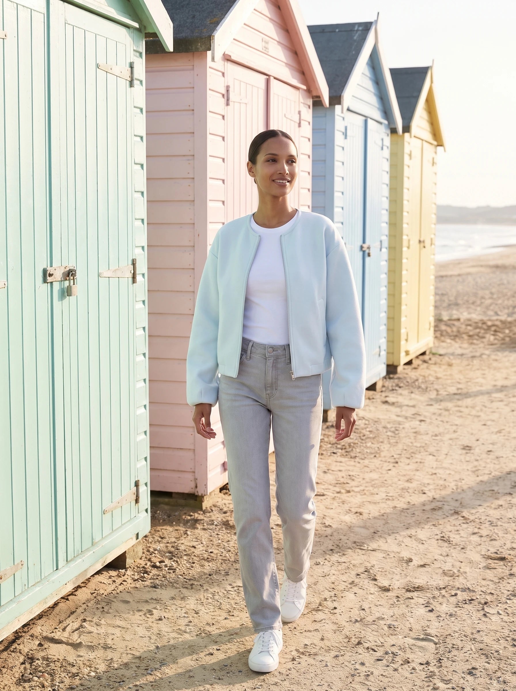 Veste zippée sans col bleu glacier Germaine, portée devant des cabines de plage pastel