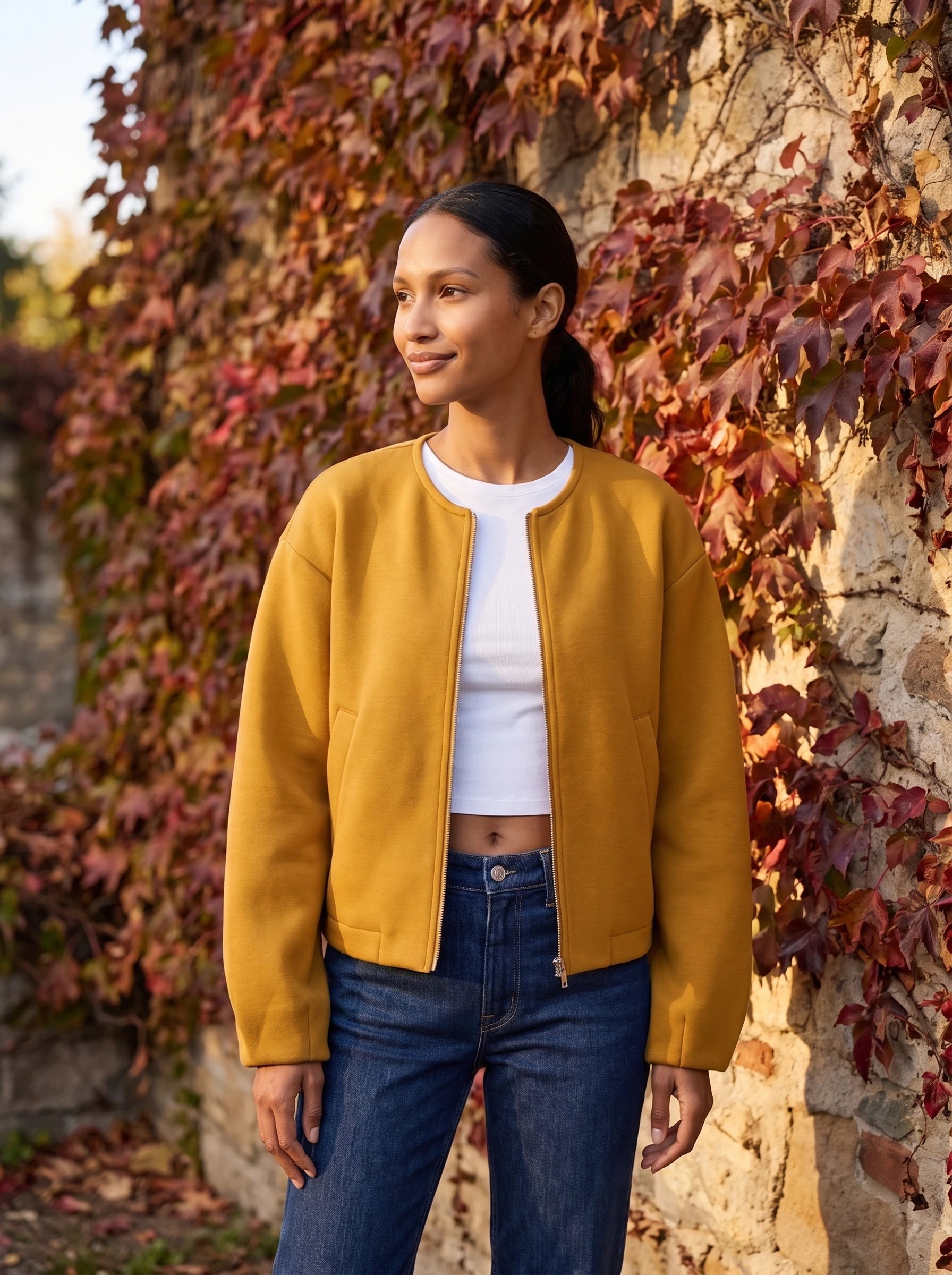 Veste zippée sans col jaune moutarde Germaine, portée devant un mur de vigne vierge rousse