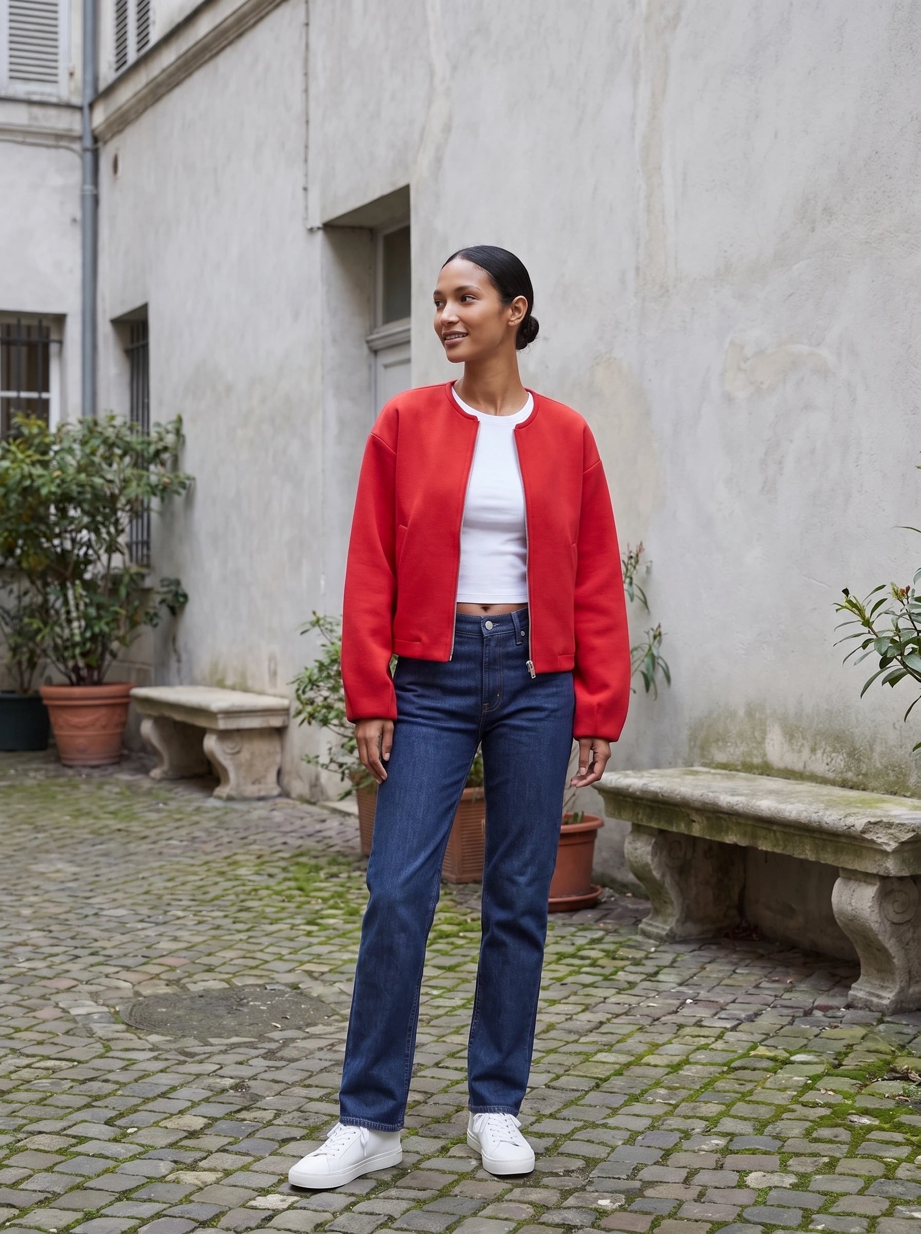 Veste zippée sans col rouge Germaine, portée dans une cour aux murs gris perle